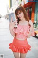 A woman in a pink top and orange skirt taking a selfie.