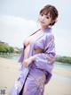 A woman in a purple kimono posing on a beach.