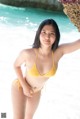 A woman in a yellow bikini standing on the beach.