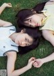 A couple of young women laying on top of a lush green field.