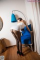 A woman in a white dress and black stockings leaning against a blue chair.