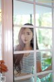 A woman standing in front of a window looking out the window.