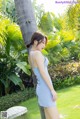 A woman in a blue dress leaning against a palm tree.