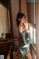 A woman in a green kimono leaning against a window.