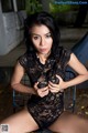 A woman in a black lace bodysuit sitting on a chair.
