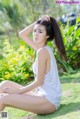 A woman sitting on the grass in a white tank top.