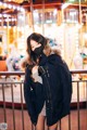 A woman wearing a face mask standing in front of a carousel.