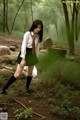 A woman in a school uniform is walking through the woods.