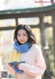 A woman wearing a pink sweater and a blue and yellow scarf.